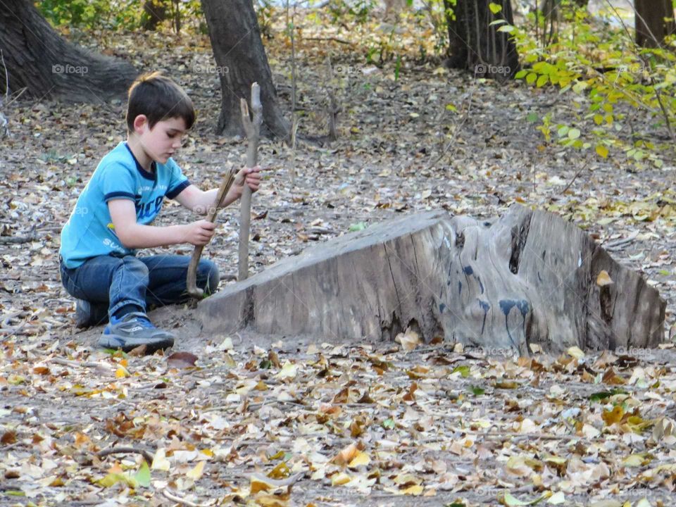A boy playing with sticks and a stump on a fall day