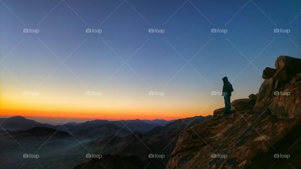 a guy standing at the very end of a cliff enjoying the view