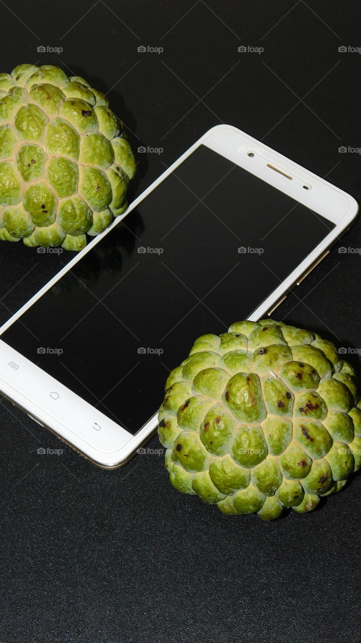 Smartphone or Android device phone with Custard apple fruits on black glazed background