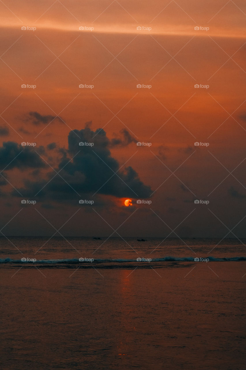 the moment when the sun goes down with a view of the beach and the waves are calming and there are 2 fishing boats far away