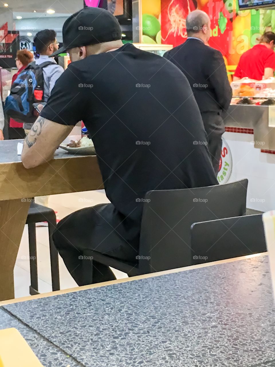 Man sitting at fast food seating in mall tattooed arm