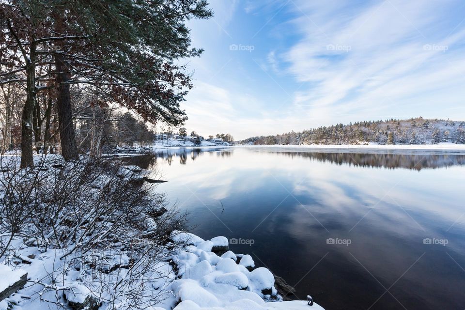Winter snowy landscape, beautiful reflection in partly frozen lake water 
