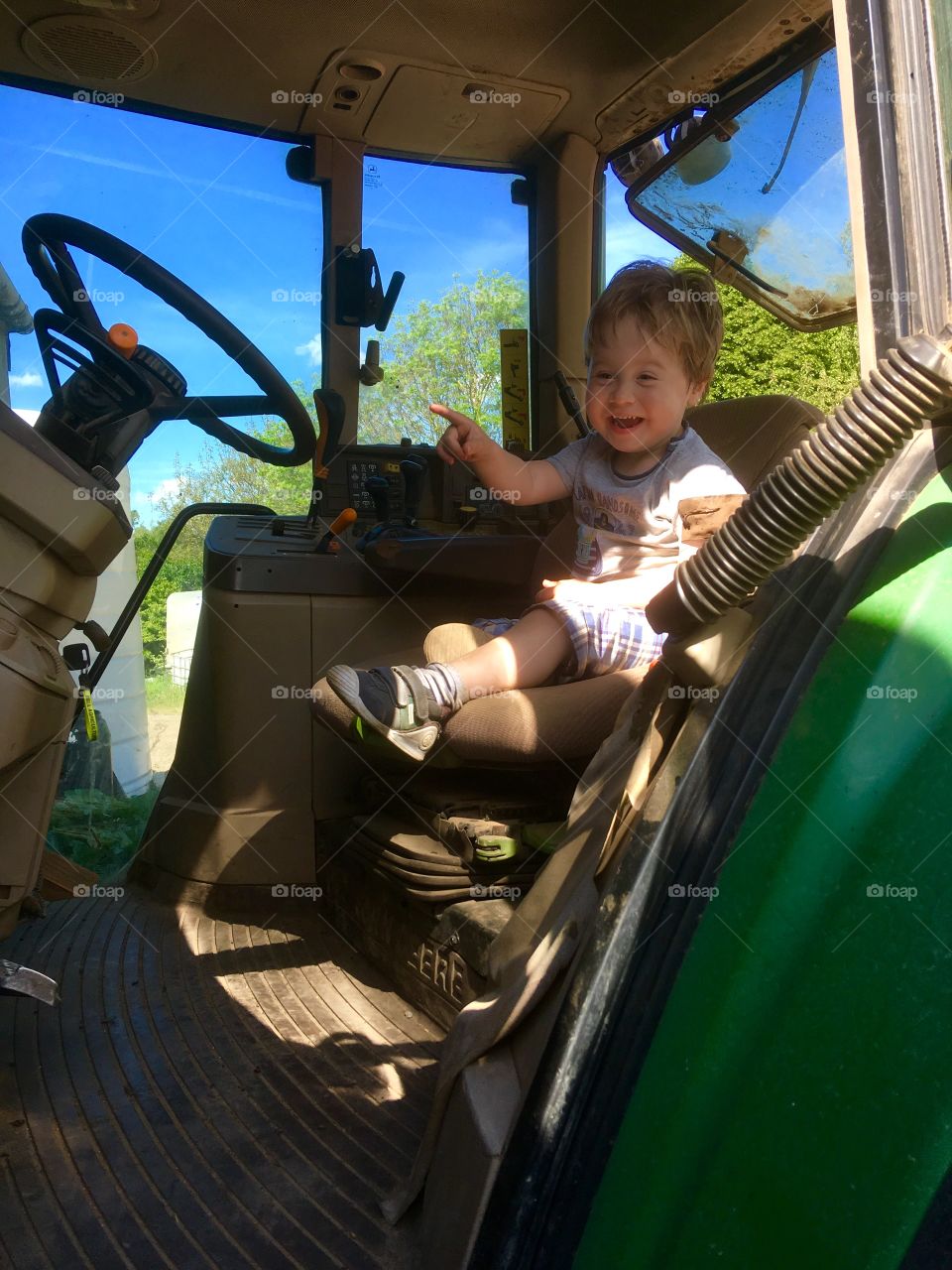 Toddler sitting in a green tractor, so pleased to be there. A genuine working tractor 