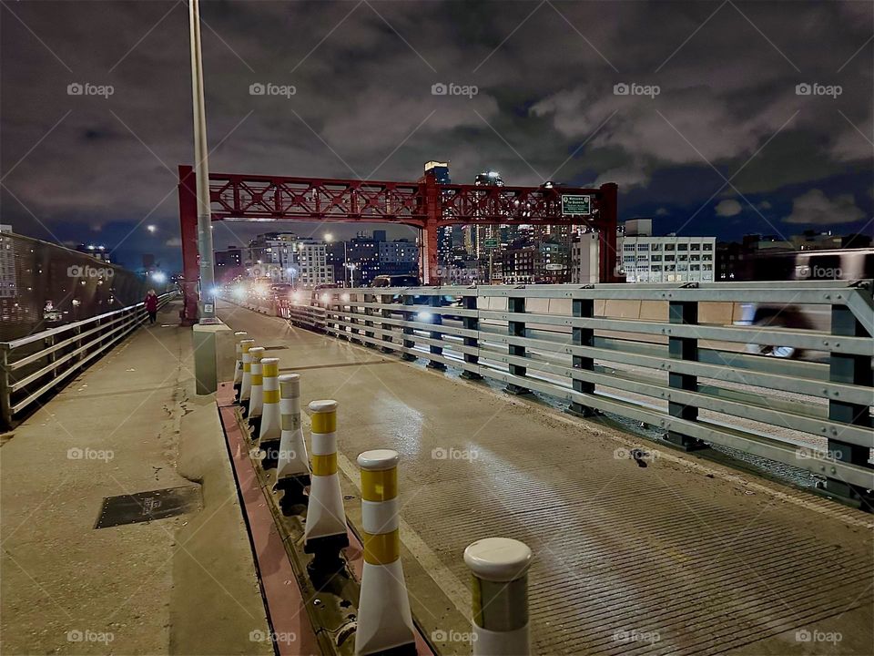 This is the “Pulaski Bridge” at “Newtown Creek” that connects “Greenpoint”, Brooklyn to LIC, Queens seen from the pedestrian lane and bicycle lane with upcoming traffic and glaring headlights. 2023. Hypnotic Productions