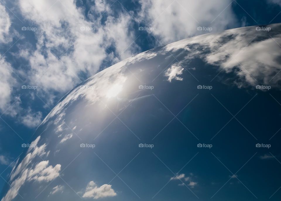 Blue clouds and fluffy white clouds reflected in a curved mirrored structure 