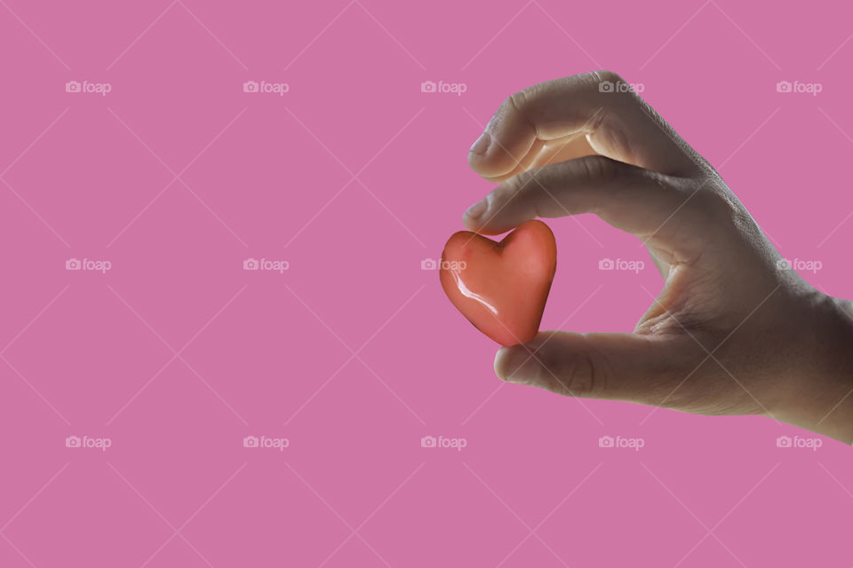 Hand holding a red candy shape heart on a pink background with clipping path for Valentine Day.