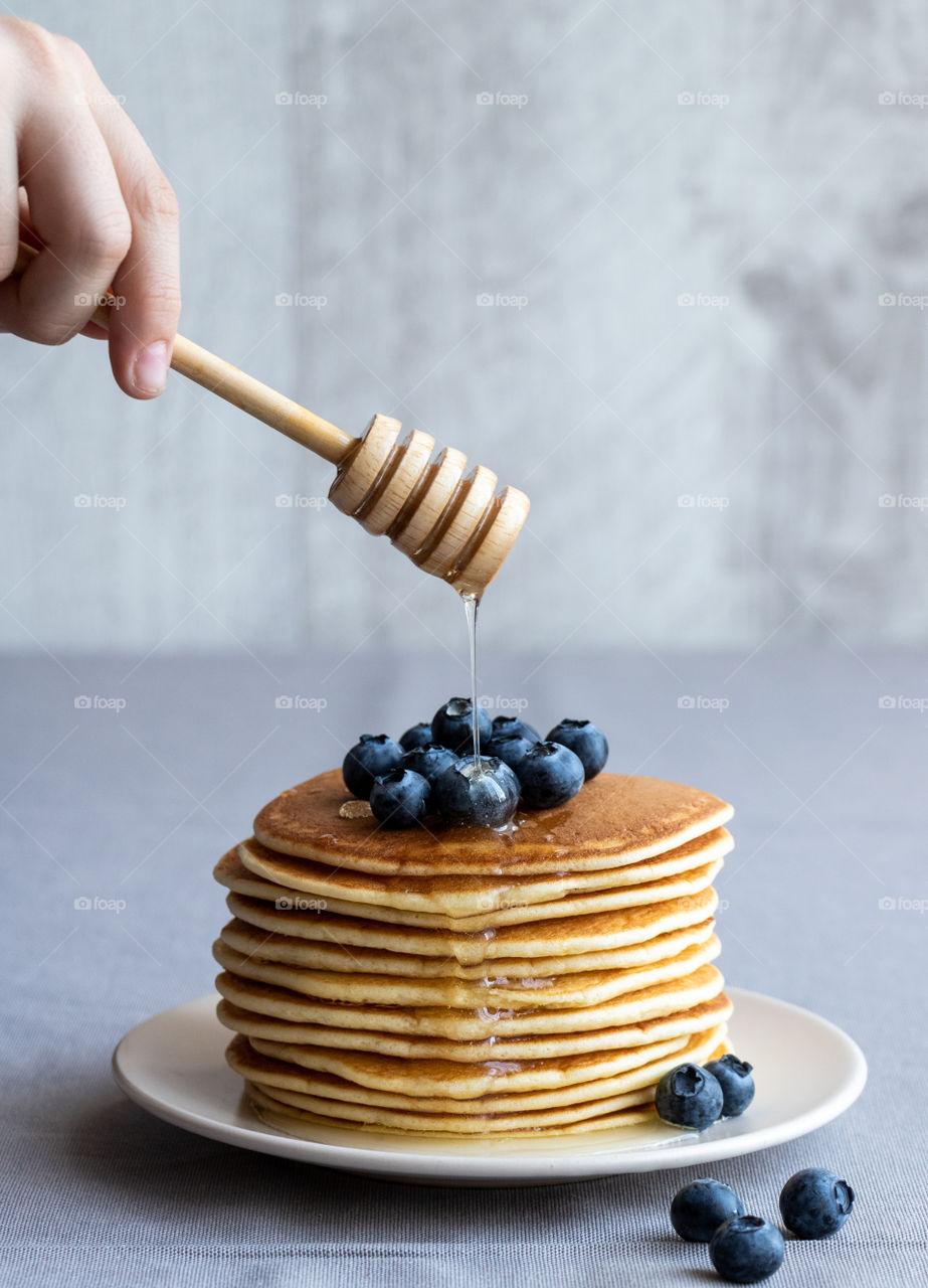 Person pouring honey on pancake and blueberries.