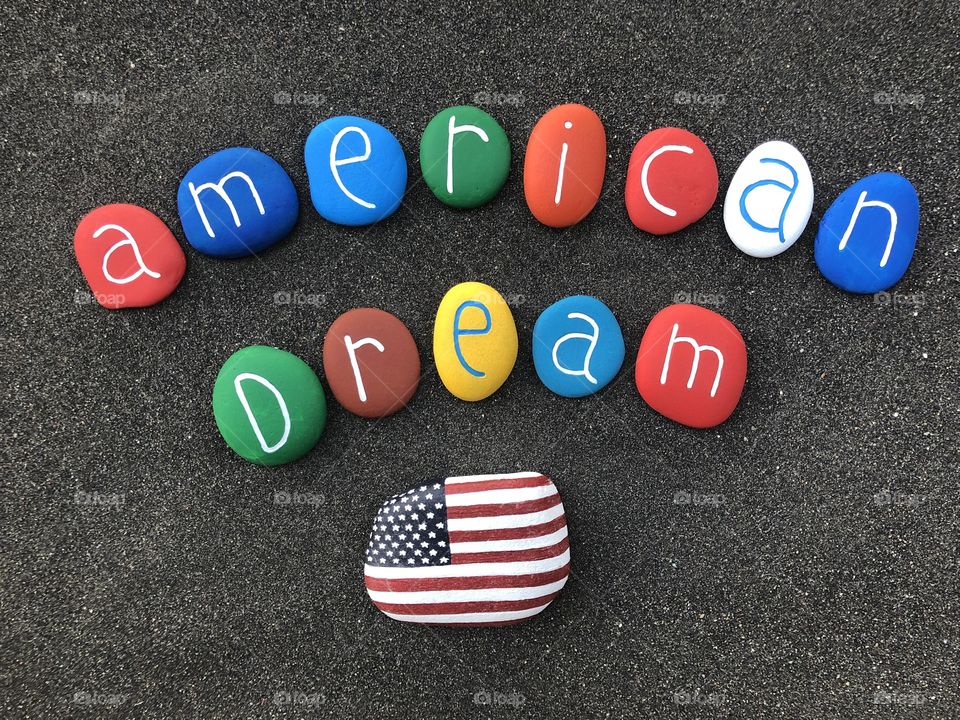 American dream text with multicolored painted sea stones over volcanic sand