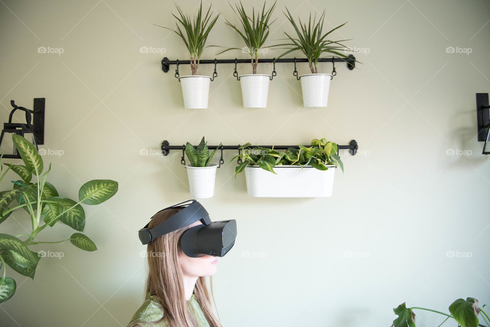 Profile of a young millennial woman wearing a virtual reality headset indoors surrounded by houseplants