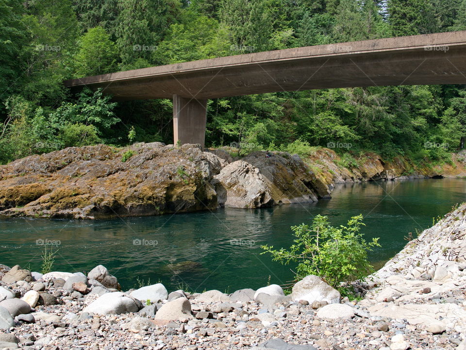 A small one-lane bridge crosses the magnificent waters of the Umpqua River and its boulder banks in Southwestern Oregon on a sunny summer morning. 