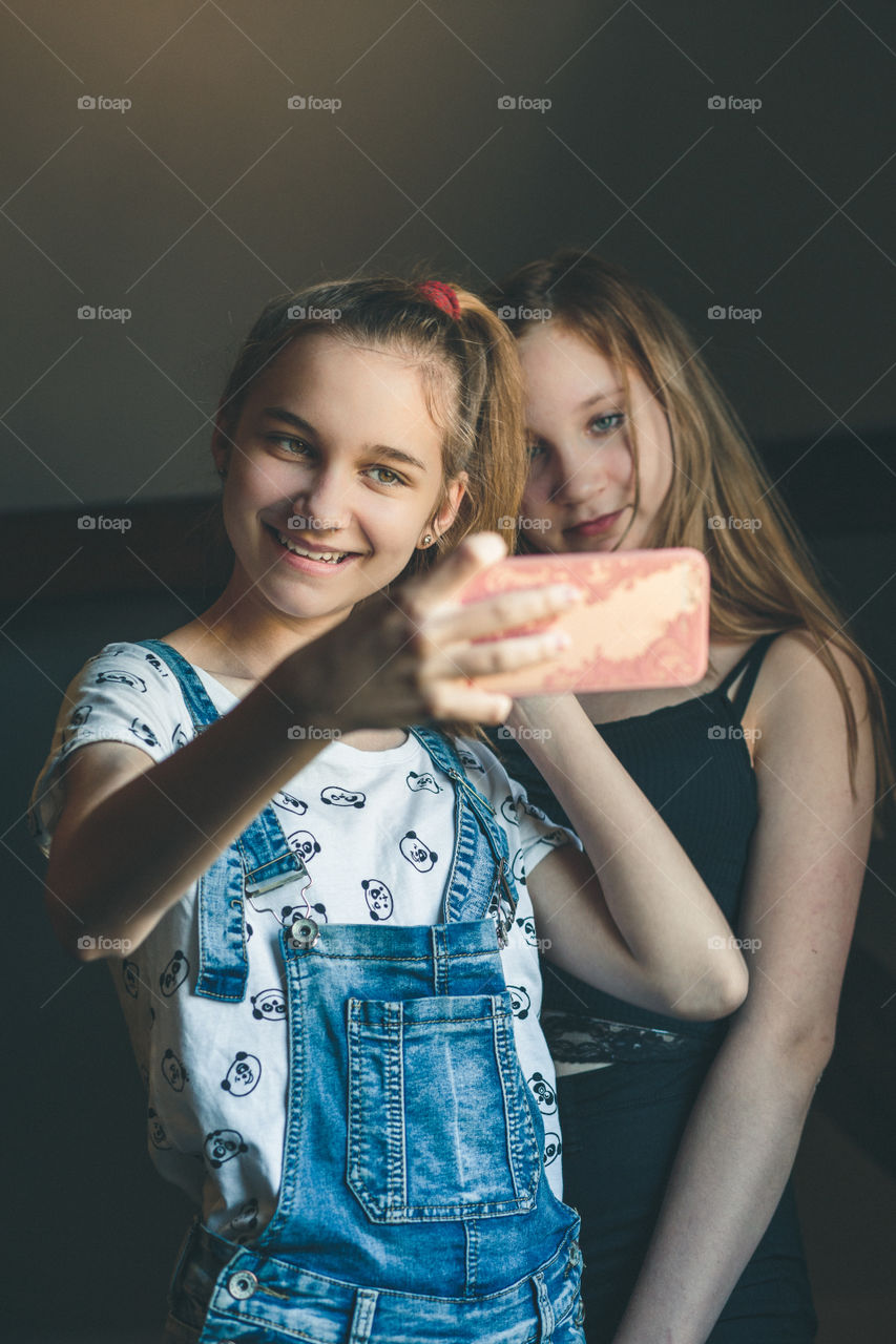 Young women taking selfie, using smartphone camera. Girls making faces, enjoying taking funny pictures together