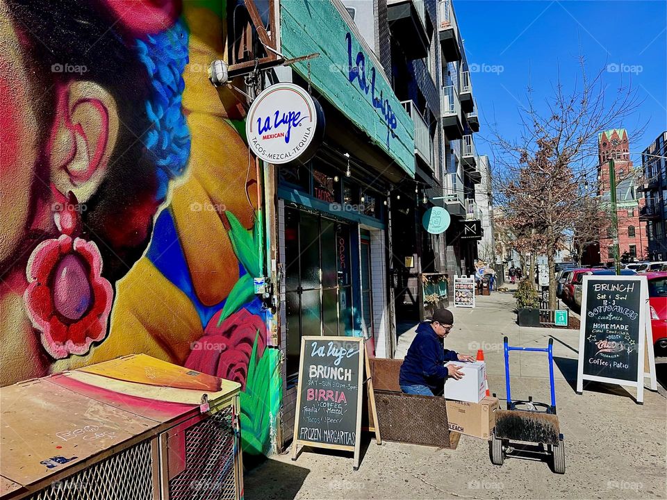 This is an indoor outdoor café on „Jefferson Street“ off „Broadway“ in „Bushwick“, Brooklyn at the end of the art mural showing the mulatto Latina. 2024. Hypnotic Productions