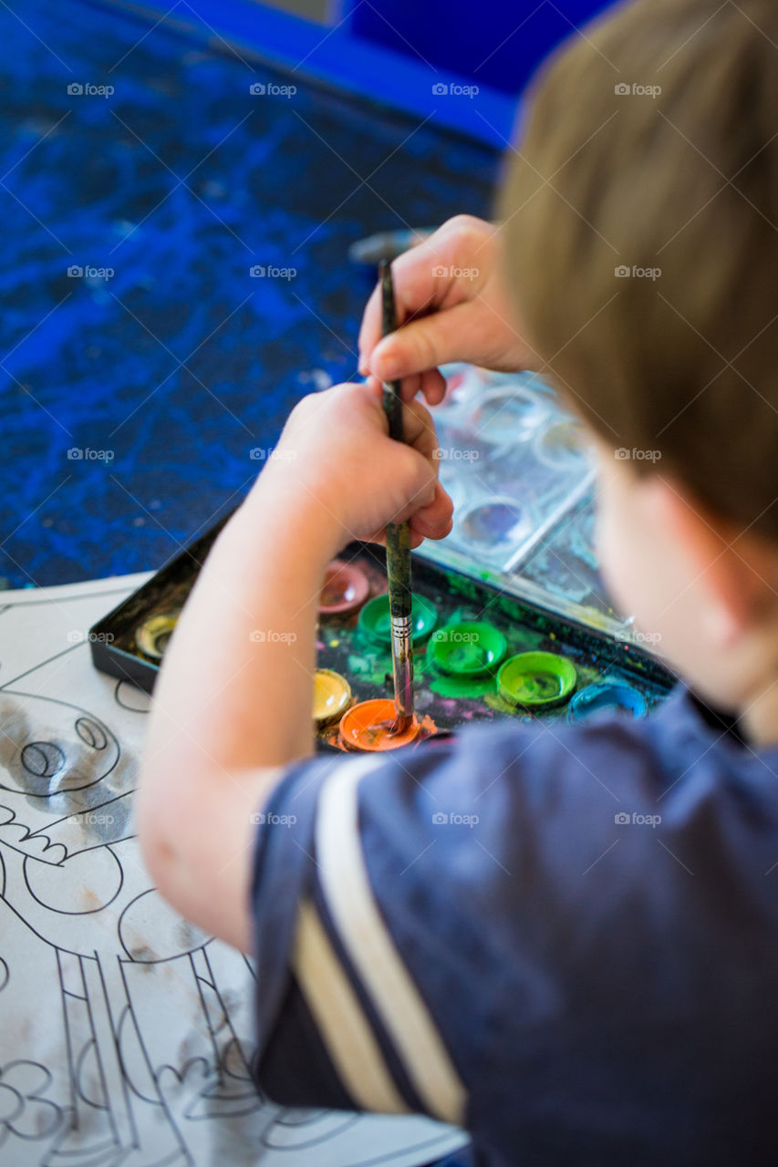 Love these colors! Image of boy using painting brush showing orange and greens, blue table in background