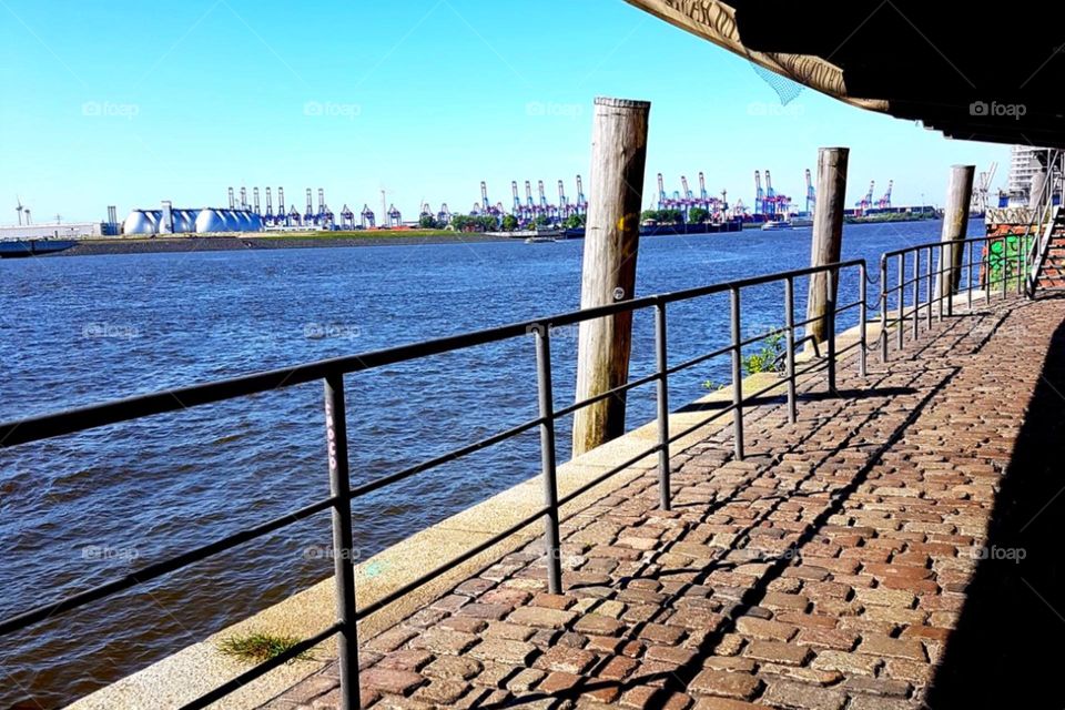 View over a railing to the blue waters of the port of Hamburg and container cranes