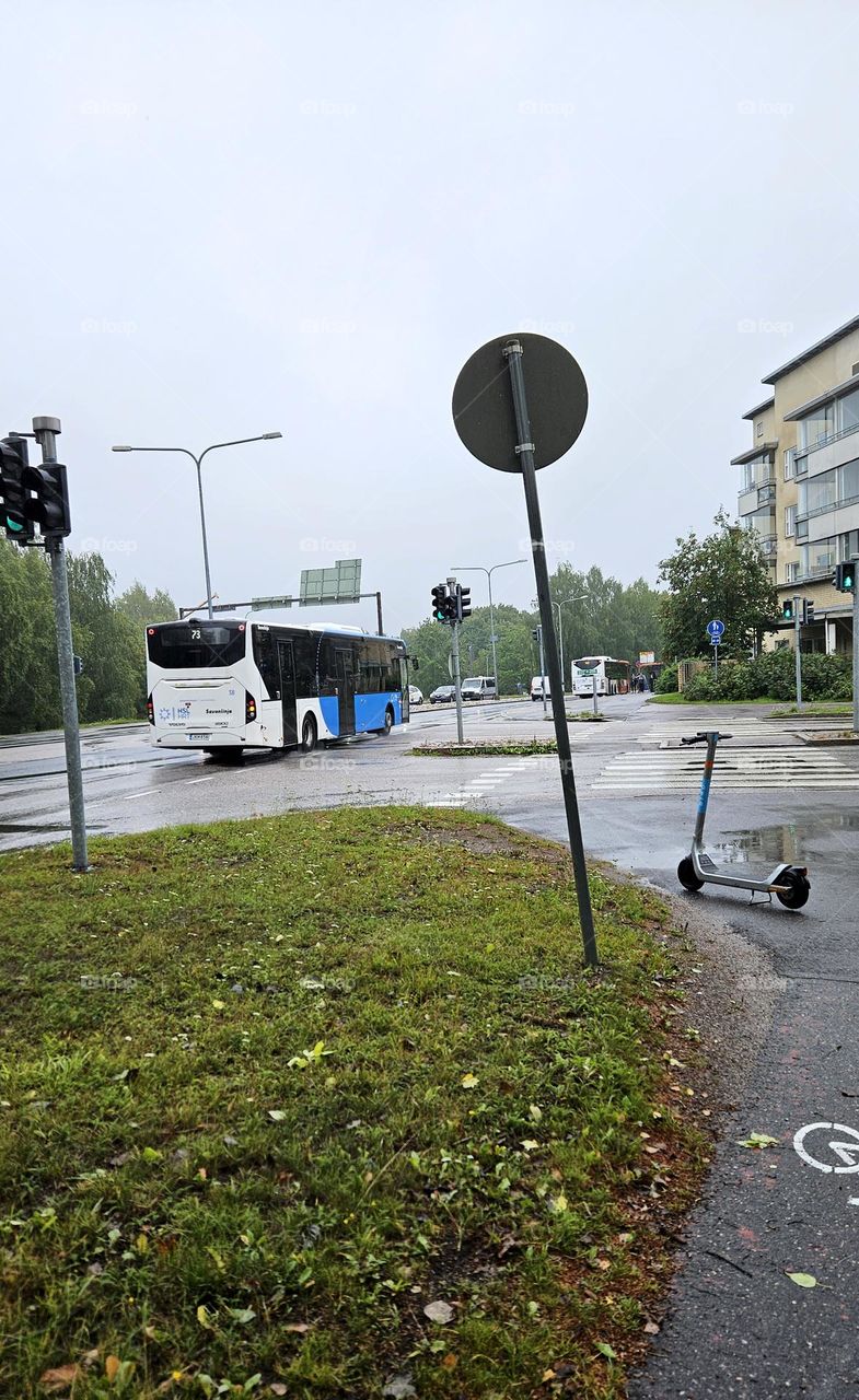 Buses are nice to travel on a rainy day. Someone has left a scooter on the footpath