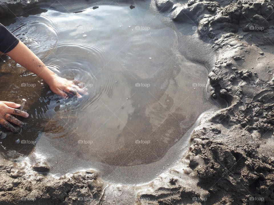 A child's hand making a hole filled with water on the beach in the morning in summer time