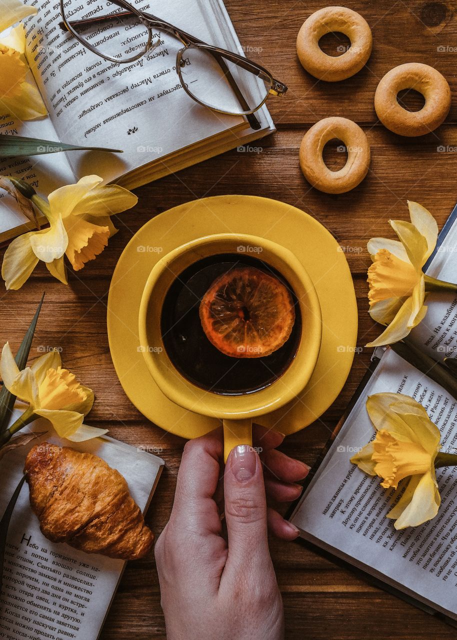 flatlay with a cup of tea, a book, flowers and croissants