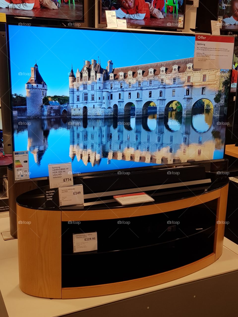 Samsung Premium 4K Ultra High Definition TV with soundbar on wood and glass TV stand with soundbar