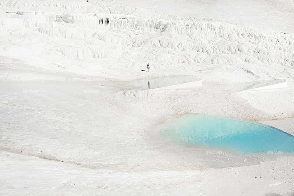 Overhead view of a tiny human walking by the white chalk mountain with blue lagoons