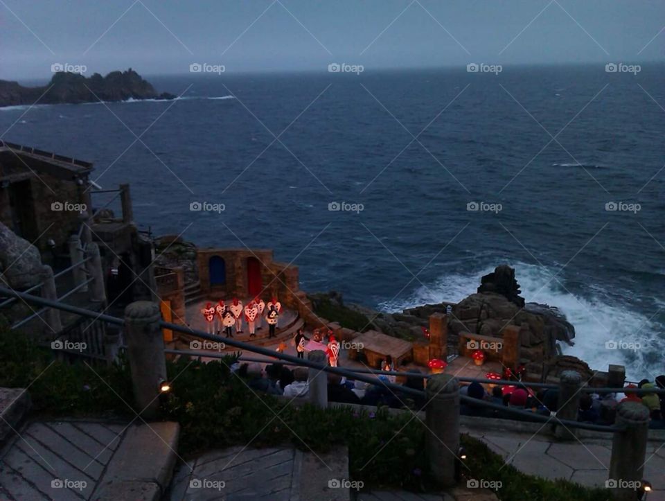 The Minack Theatre
Alice in wonderland performance
(Cornish: Gwaryjy Minack) is an open-air theatre, constructed above a gully with a rocky granite outcrop jutting into the sea (minack from Cornish meynek means a stony or rocky place). The theatre is at Porthcurno, 4 miles (6.4 km) from Land's End in Cornwall, England. The season runs each year from May to September, and by 2012 some 80,000 people a year see a show, and more than 100,000 pay an entrance fee to look around the site. It has appeared in a listing of the world's most spectacular theatres.