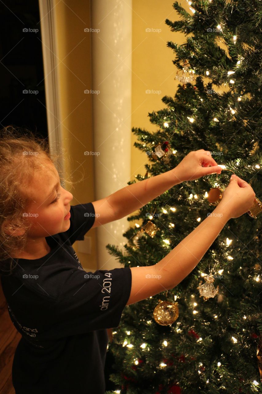 Child, girl hanging Christmas ornaments on tree