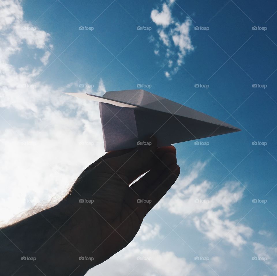 Person holding paper plane against sky