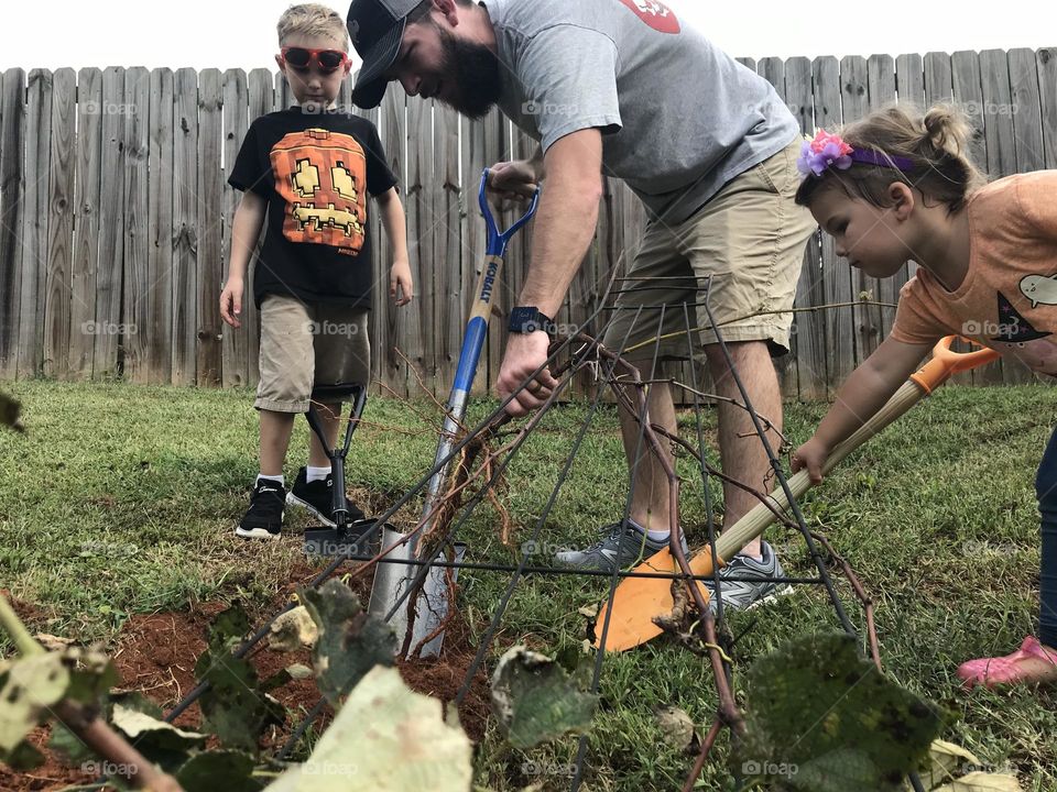 A dad doing yard work with his children. 