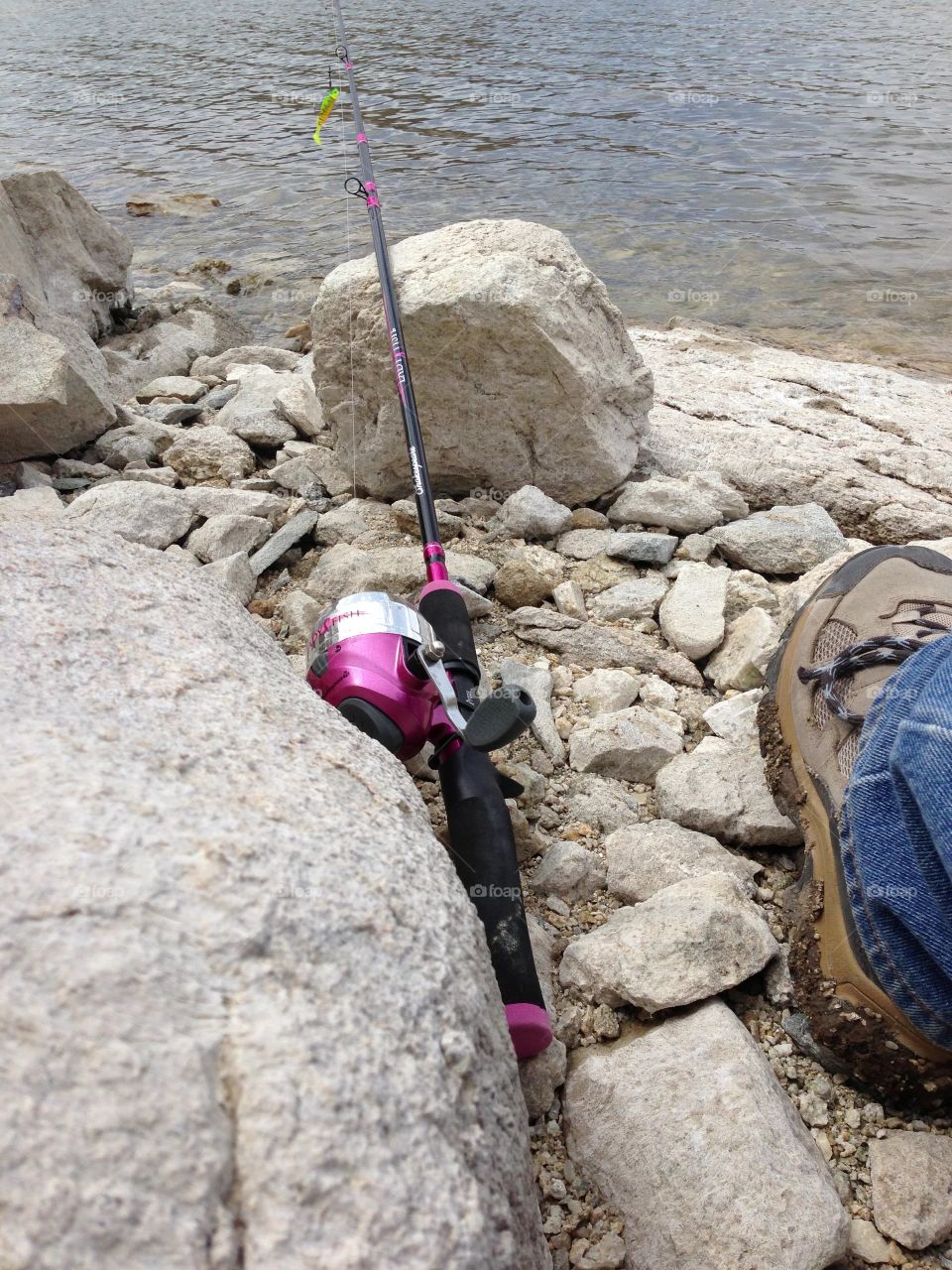 Girl Fishing. Bright pink fishing pole on the rocks of the lake shore