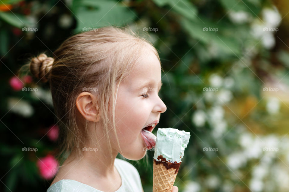 Little girl with blonde hair licking ice cream 