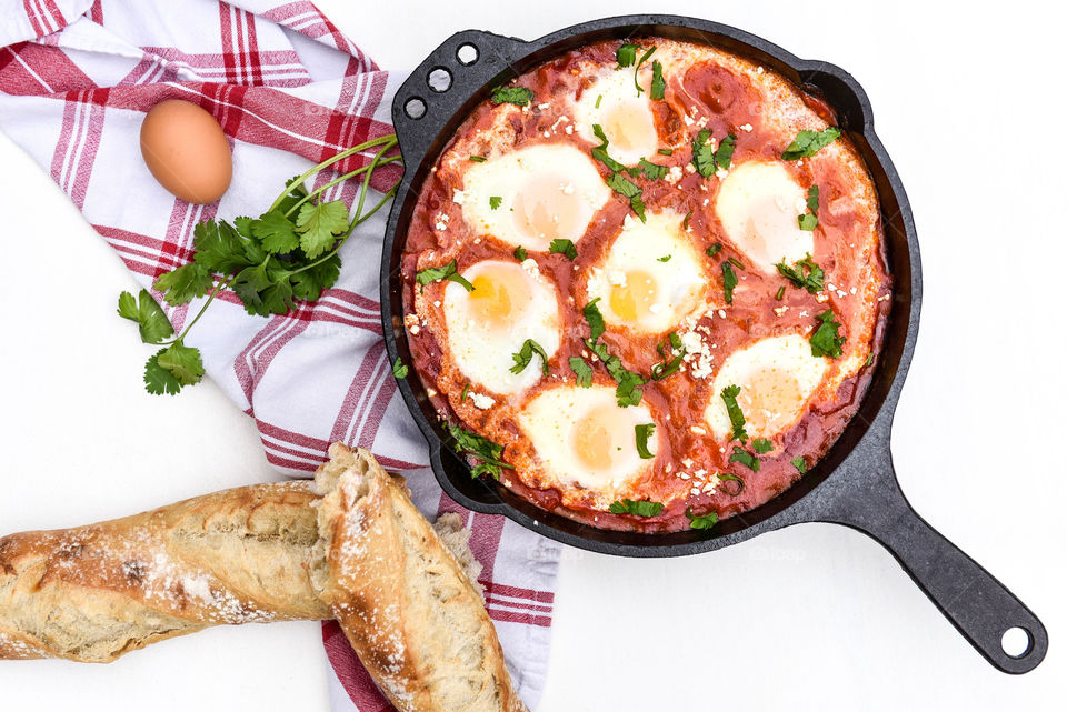 Flat lay of a prepared shakshouka dish in a cast iron skillet surrounded by ingredients
