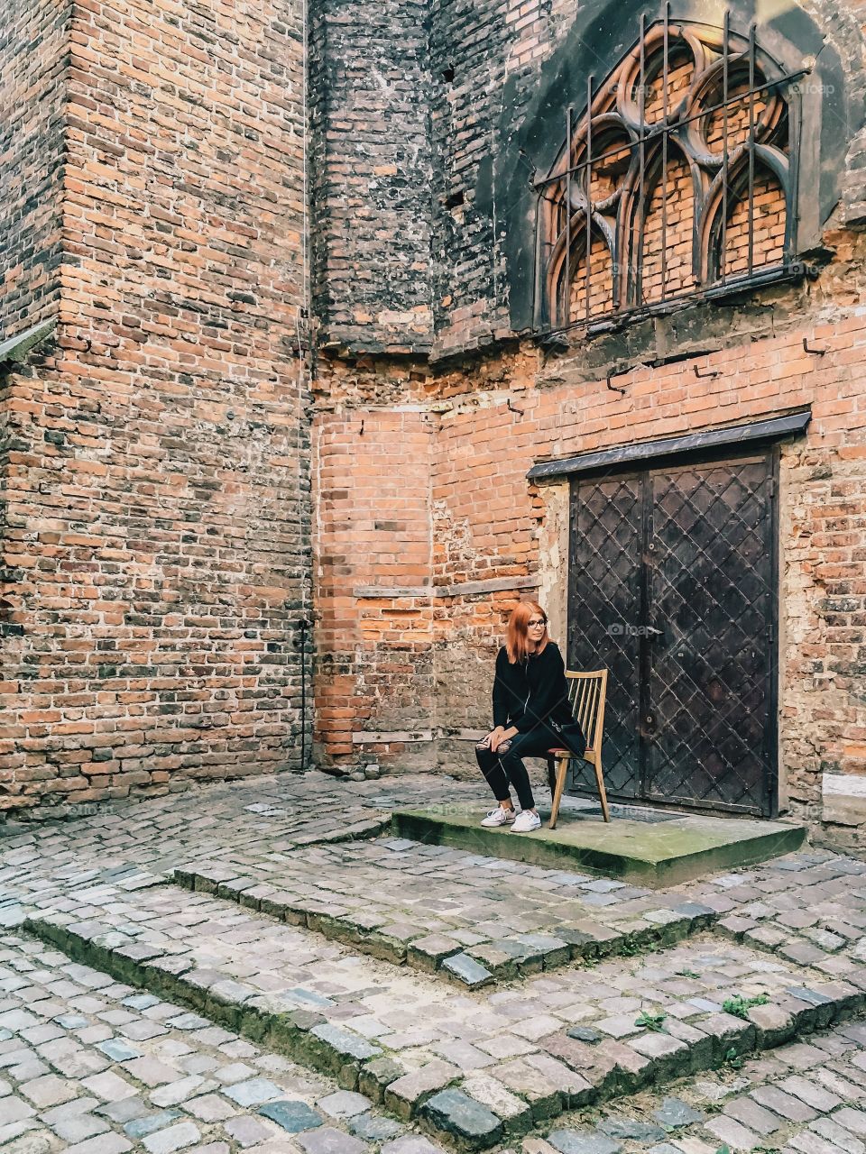 Beautiful woman sitting on chair against brick wall of old building