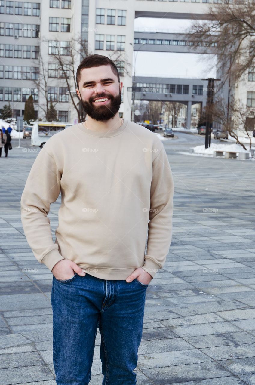 Portrait of happy, smiling, friendly bearded young man in casual clothes walking in city street in winter. Ukraine