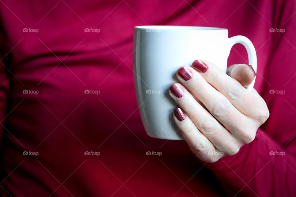 Woman's hand with beautiful manicure is holding a white cup