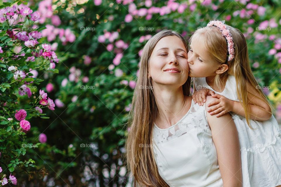 Beautiful little Caucasian girl with blonde hair kissing her mother outdoor at summer 