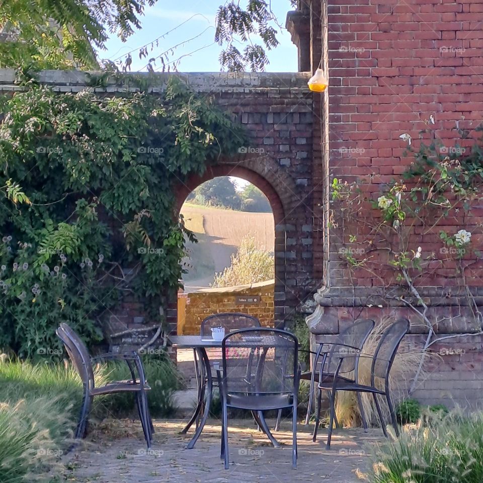 pretty empty outside dining. natural view through archway summer afternoon table and chairs.