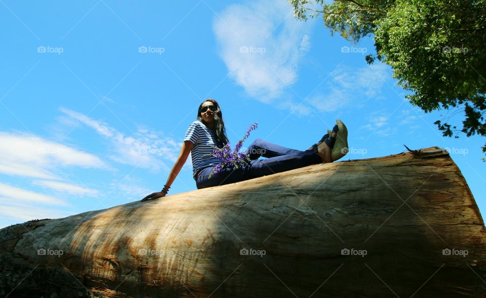 Girl sitting on the tree bark in the background of blue sky