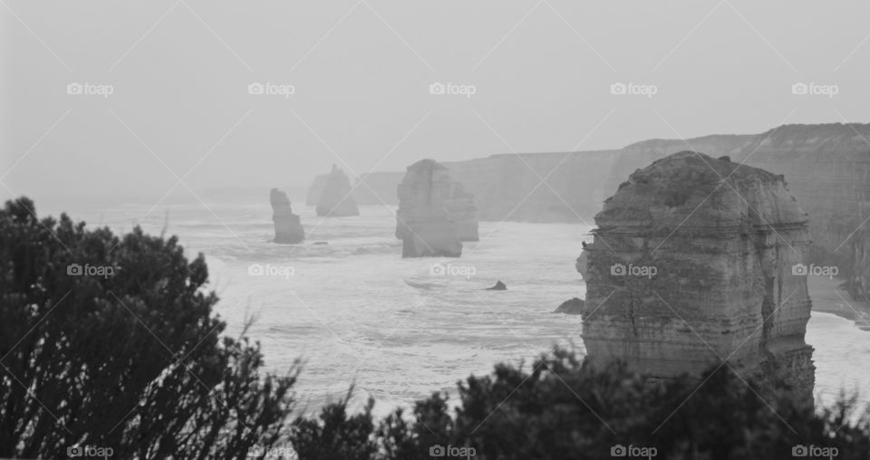 Rocky cliffs losing a war against the sea. Misty foggy ocean landscape.