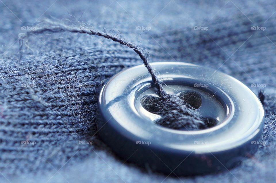 Round blue button with a loose thread on a shirt 