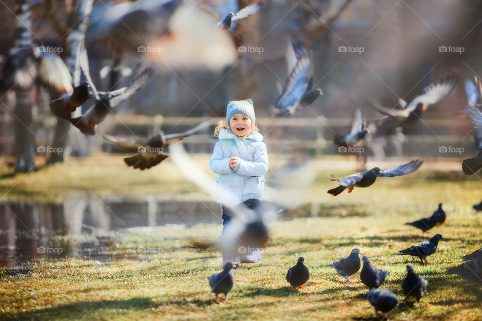 Little girl with pigeons in spring park.