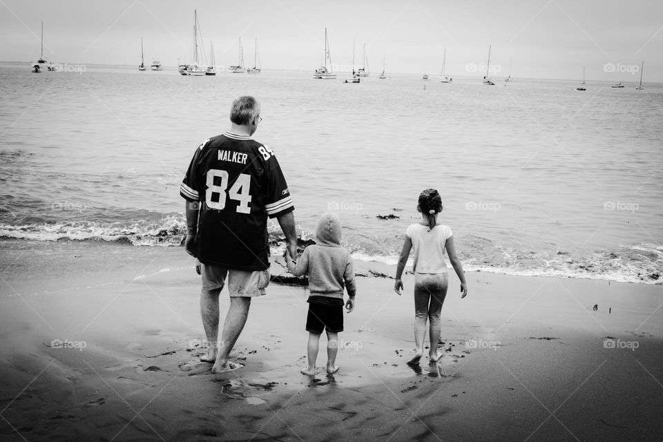 Father and his kids walking on the beach towards the water together as a family 