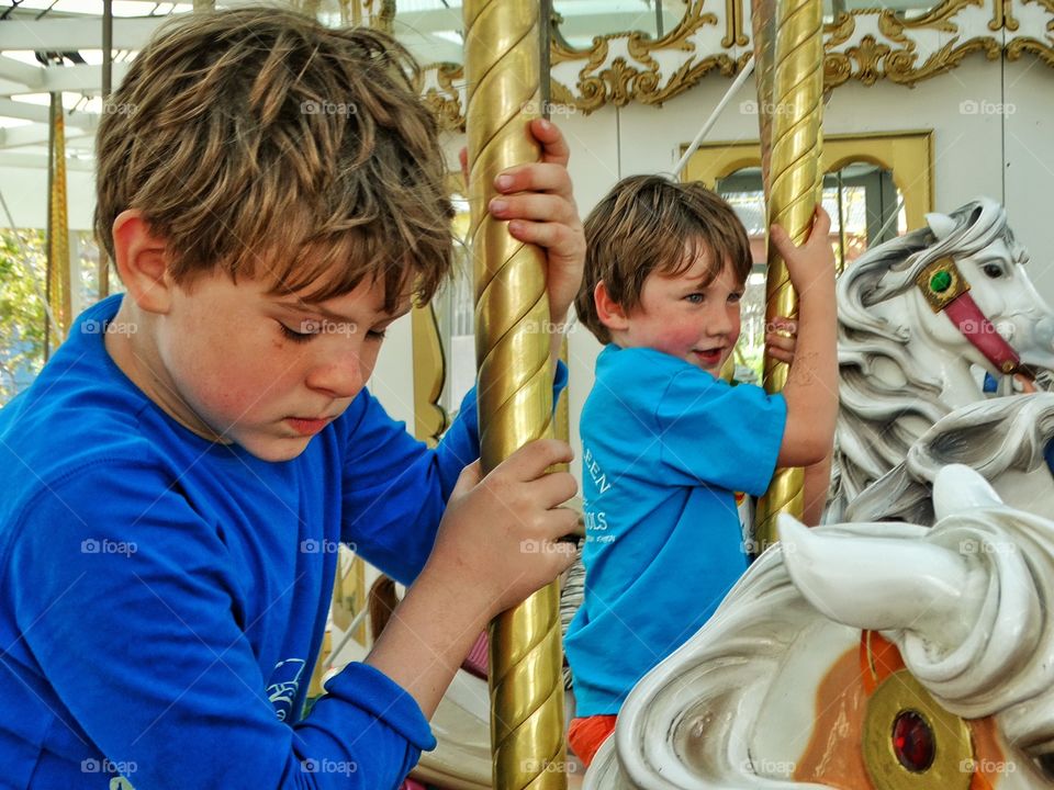 Boys Riding A Carousel. Young Brothers Riding Toy Horses On A Vintage Carousel