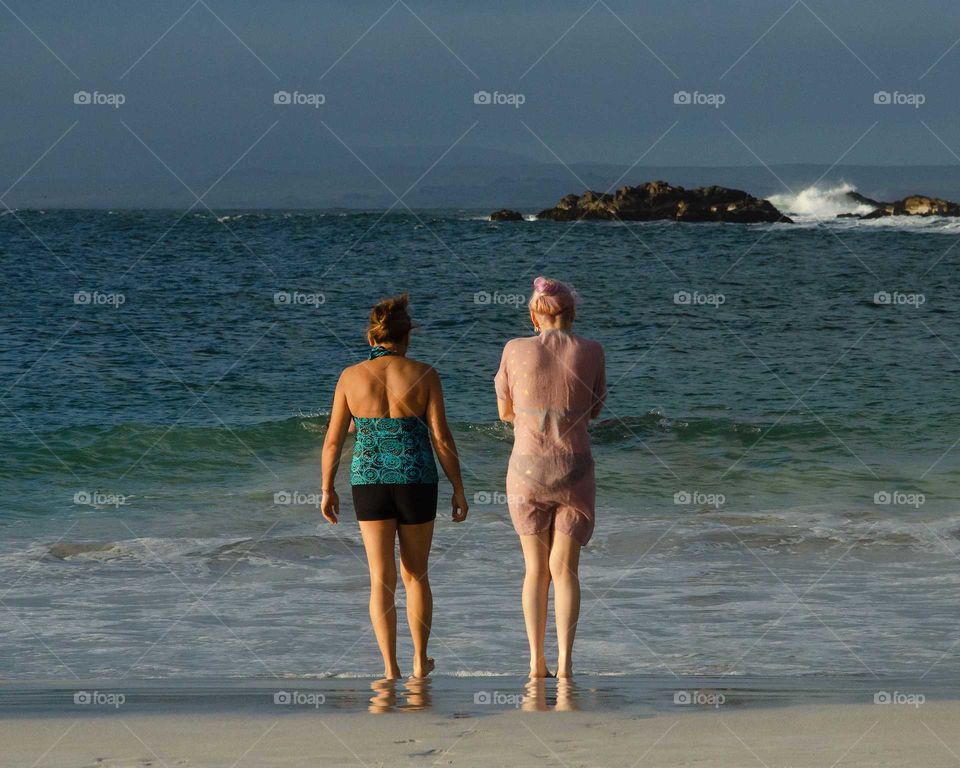 two young women standing in front of the beach looking at the sea