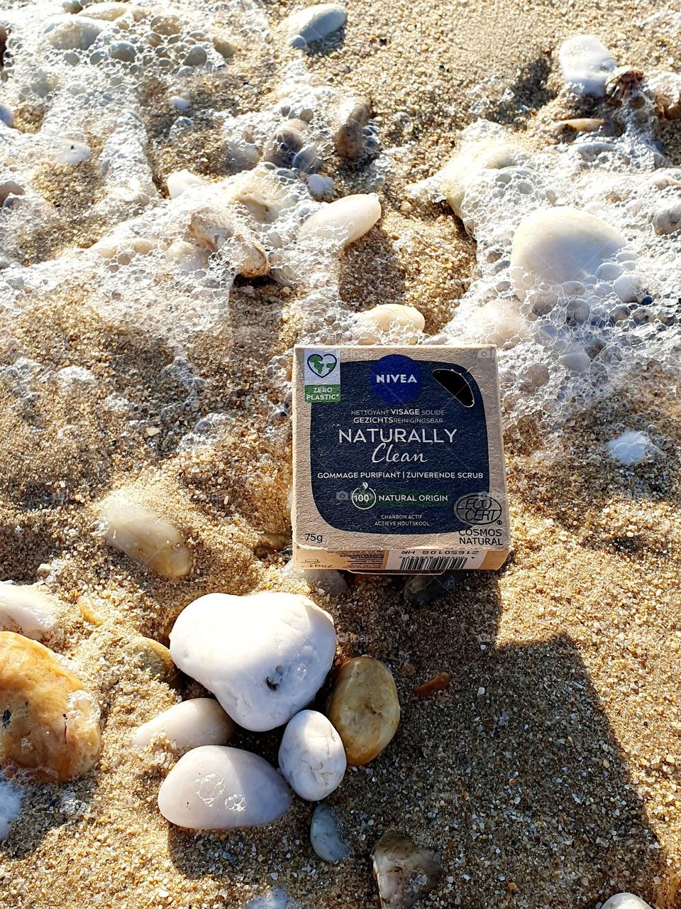 Nivea Naturally Clean soap box placed on beach sand and surrounded by beach pebbles and sea foam