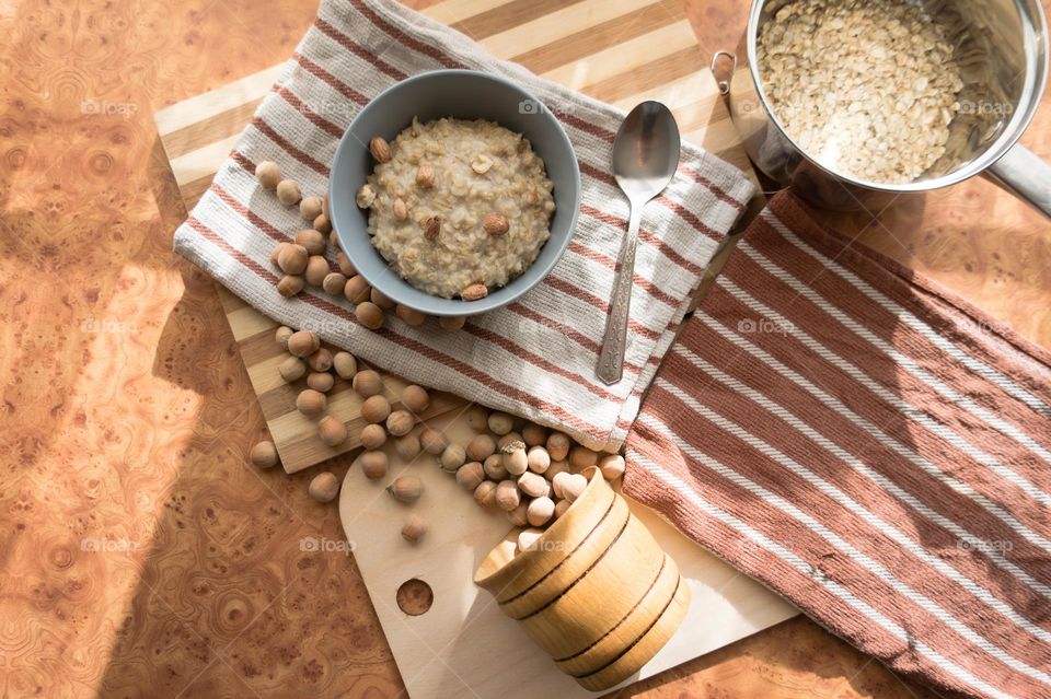 Cooked oatmeal in a deep gray plate with hazelnuts and honey.