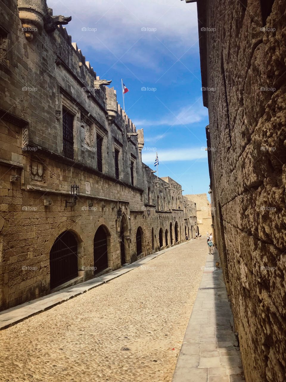 the road is covered with pebbles, 2 sides are the wall is magnificent , some people are walking in the distance . Blue sky ,  white clouds , a very beautiful sunny day