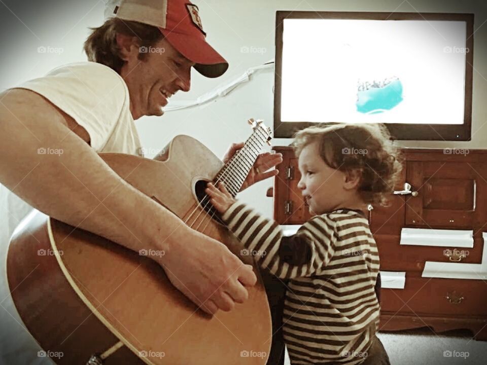 A father plays guitar with his toddler son