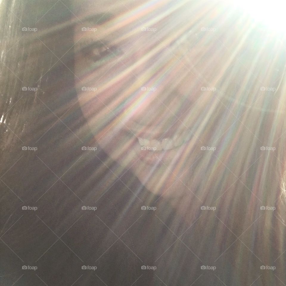 Woman smiling in background as the sun peaks through creating a sun ray shining halo