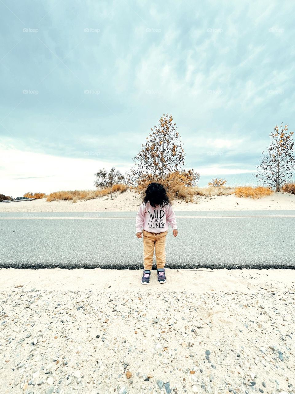 Little girl stands by the road, standing in the sand by the roadway, roads by the beach 