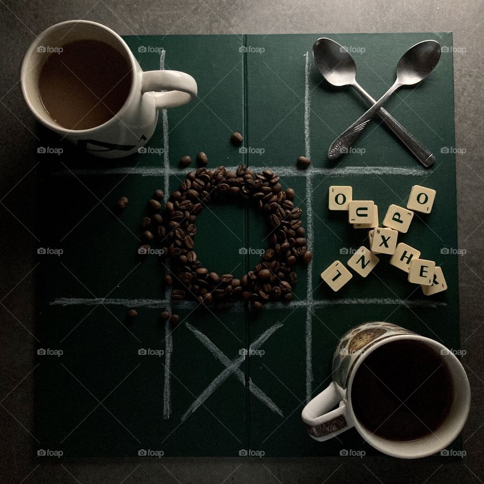 Noughts and crosses (tic-tac-toe) board game flatlay with scrabble and coffee.