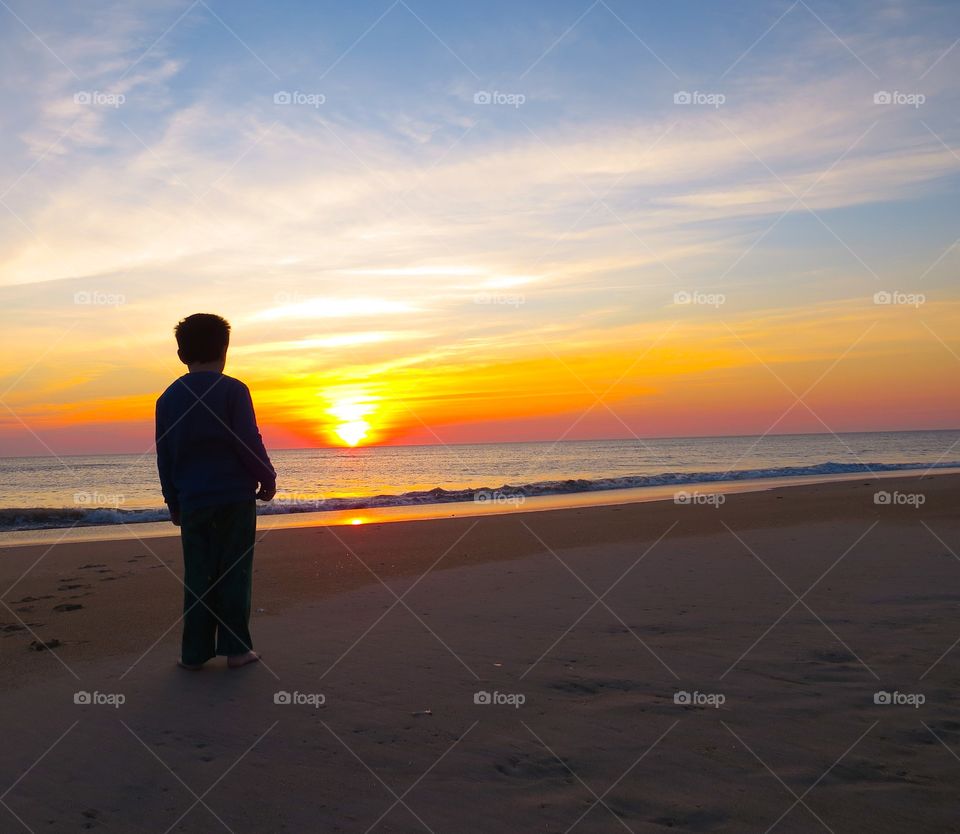 Little boy watching the sunrise at the beach.